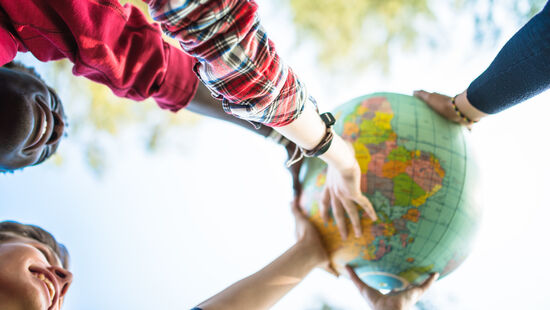 Junge Menschen halten einen Globus in den Himmel. Foto: Getty Images