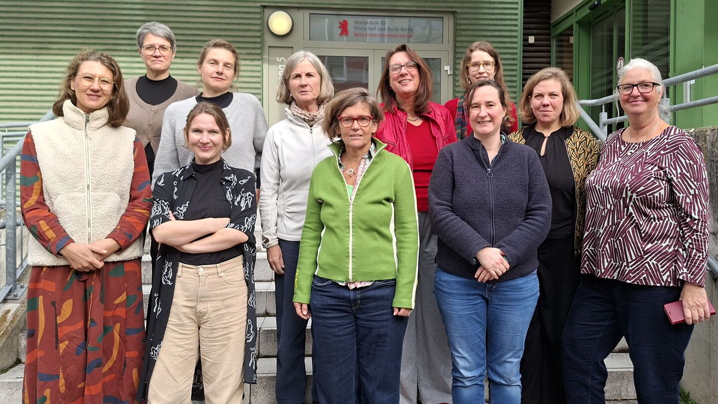 Gruppe Frauen unterschiedlichen Alters steht auf einer Außentreppe vor einem Gebäude mit grün gestrichener Fassade