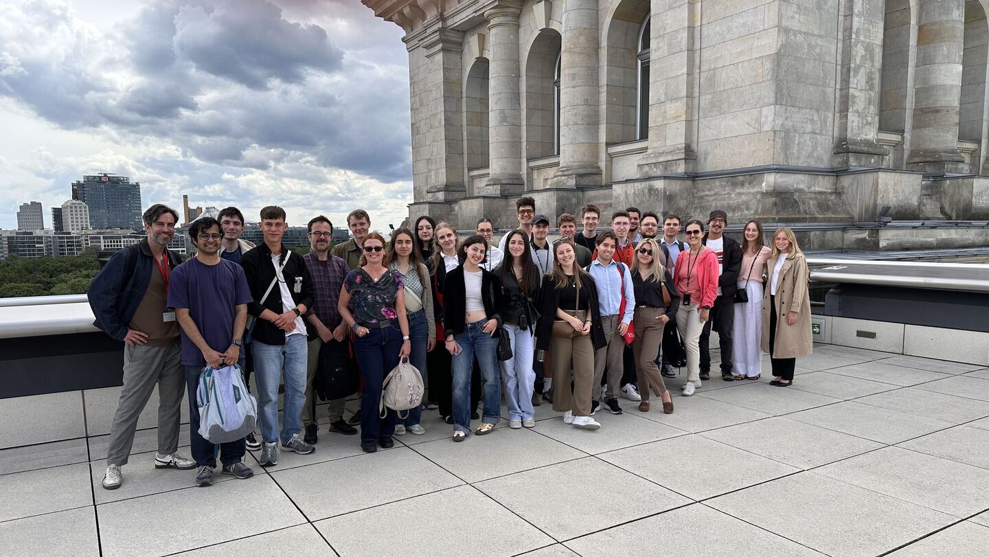 Group of people standing on a large terrace in front of a historic building with columns under a cloudy sky