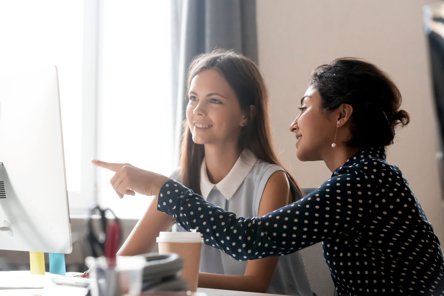 Bewerbung duales Studium Fachbereich Allgemeine Verwaltung: Dual Studierende sitzt im Büro einer Behörde mit ihrer Kollegin vor dem Rechner und diskutiert. Foto: © fizkes/ Getty Images/ iStockphoto