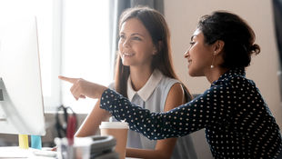 Bewerbung duales Studium Fachbereich Allgemeine Verwaltung: Dual Studierende sitzt im Büro einer Behörde mit ihrer Kollegin vor dem Rechner und diskutiert. Foto: © fizkes/ Getty Images/ iStockphoto