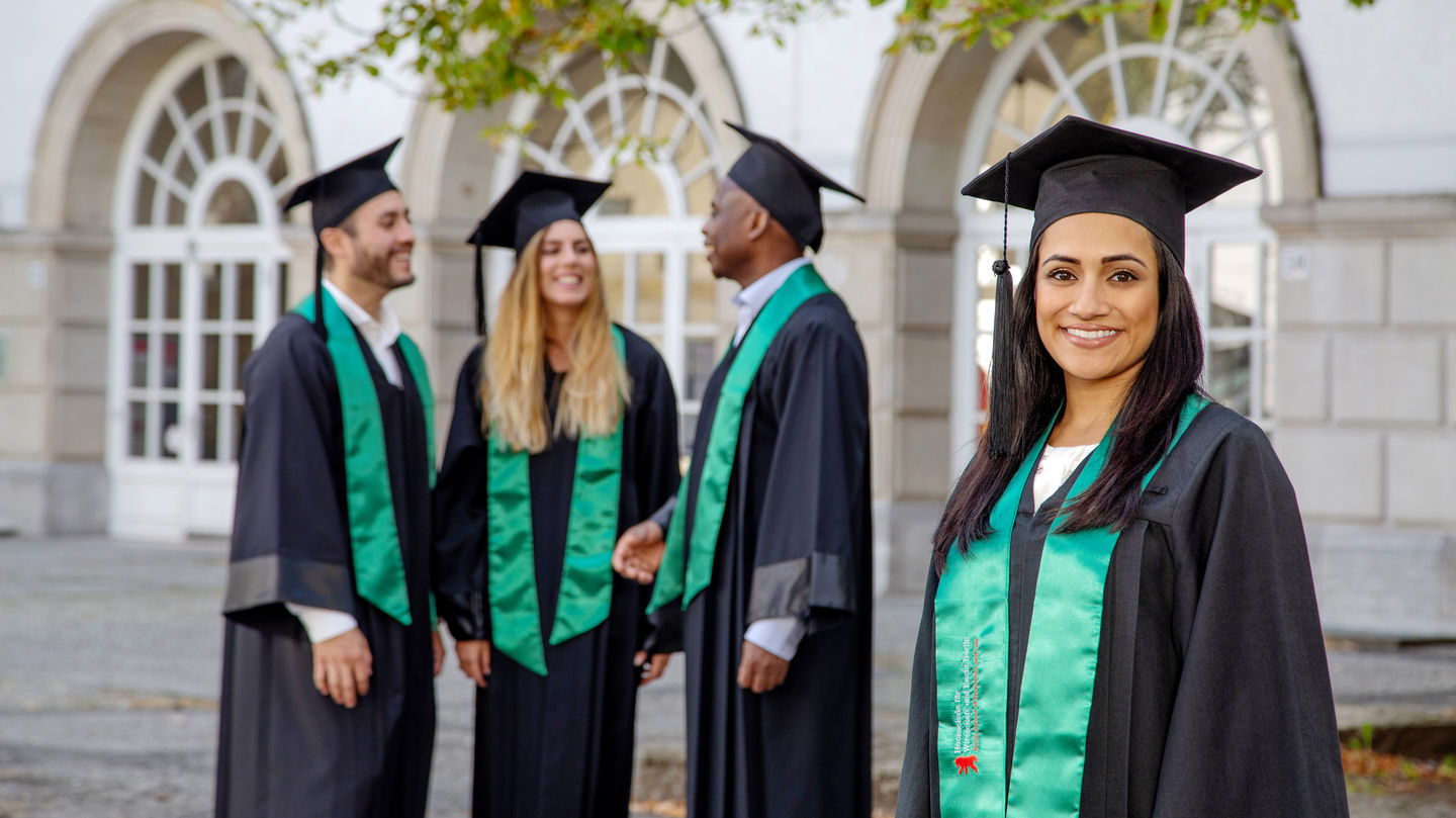 Studierende der MBA-Programme an der Berlin Professional School profitieren von einem großen internationalen Netzwerk aus Unternehmen und Hochschulen weltweit. Online-Info-Session zum Berlin MBA am 18. März 2022 ab 18 Uhr. Foto: Katy Otto Vier Studierende im Talar stehen vor einem hellem Gebäude.