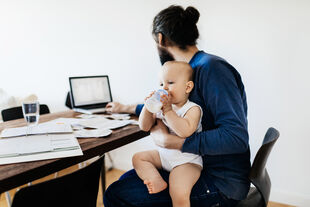 Illustration: Student mit Baby auf Schoß vor dem Laptop