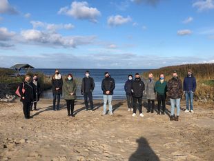 Gruppe von Menschen am Strand mit MNS und Abstand zueinander.