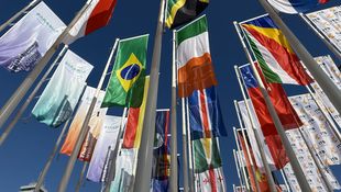 Mehrere Fahnen verschiedener Länder wehen an Fahnenmasten vor blauem Himmel