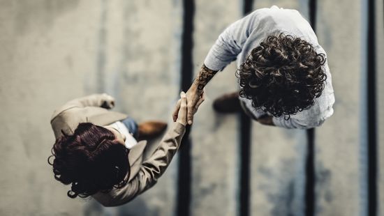 Kameraperspektive von oben: Ein Mann und eine  Frau schütteln sich die Hand. Foto: © nimis69/E+/Getty Images