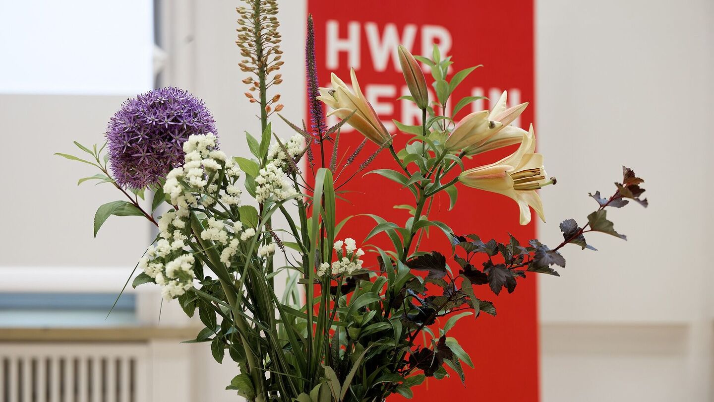 Strauß aus verschiedenen Blumen vor rotem Banner mit weißer Schrift