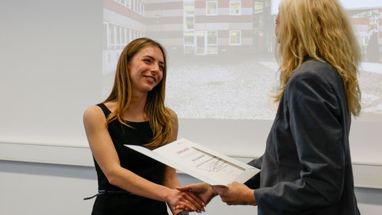 Eine Frau schüttelt einer anderen die Hand und übergibt eine Auszeichnung.