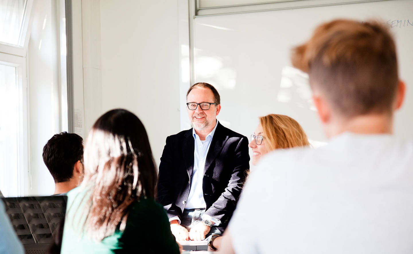 Studieren an der HWr Berlin: Lächelnder Professor mit Brille diskutiert mit einer Gruppe Studierender.