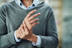 Hände aus der Nähe: Ein Mann greift sich mit der linken Hand ans rechte Handgelenk. Foto: © LaylaBird/Getty Images/iStockphoto