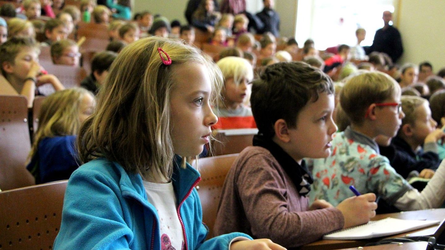 Noch bis zum 27. November halten echte Professorinnen und Professoren von HWR Berlin und HTW Berlin an der KinderUni Lichtenberg spannende Vorlesungen für neugierige Kinder ab 8 und die ganze Familie. Foto: Sylke Schumann Kinder in einem Hörsaal.