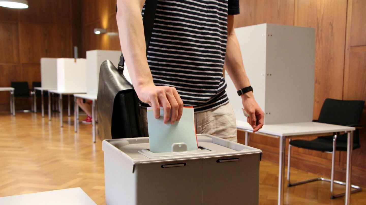 Person wirft Stimmzettel in schmalen Schlitz der Wahlurne.