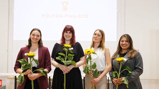 Vier Frauen stehen nebeneinander und halten jeweils eine Sonnenblume vor einem weißen Hintergrund mit der Projektion 'POLITEIA-Preis 2025'