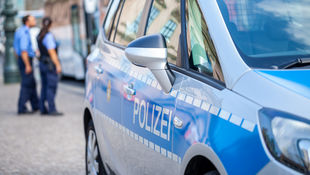 Berliner Polizeiauto auf der Straße. Im Hintergrund sind eine Polizistin und ein Polizist in Uniform zu sehen. Foto: © huettenhoelscher/iStock/Getty Images Plus