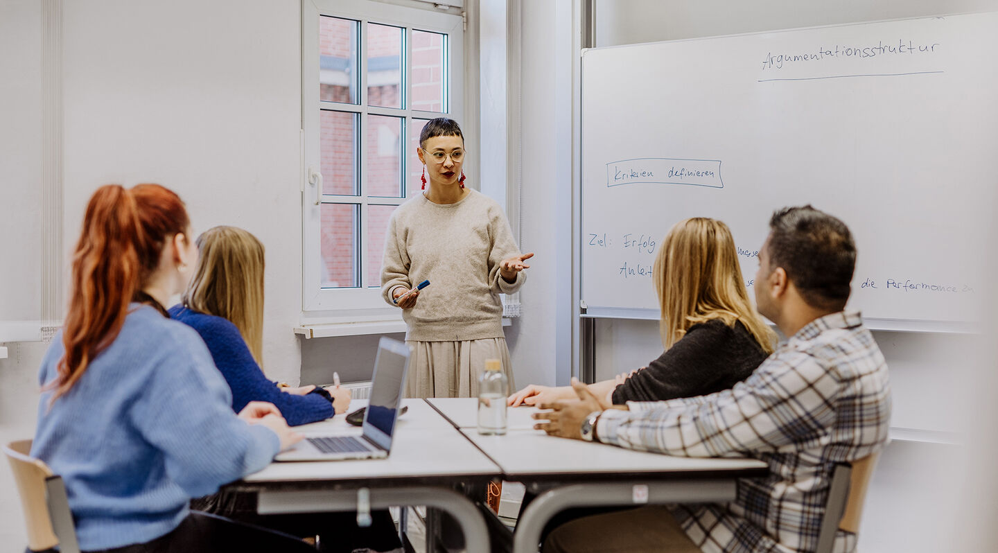 Wissenschaftliches Schreiben: Vier Studierende sitzen an einem Tisch und schreiben per Hand oder am Laptop. Foto: © fotostorm/ Getty Images/ E+