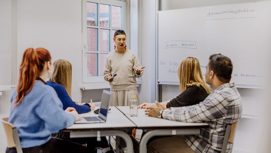 Wissenschaftliches Schreiben: Vier Studierende sitzen an einem Tisch und schreiben per Hand oder am Laptop. Foto: © fotostorm/ Getty Images/ E+