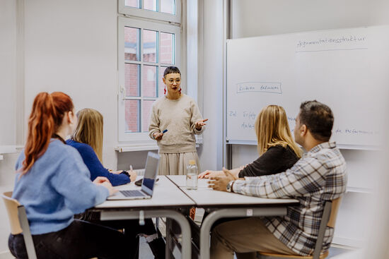 Wissenschaftliches Schreiben: Vier Studierende sitzen an einem Tisch und schreiben per Hand oder am Laptop. Foto: © fotostorm/ Getty Images/ E+