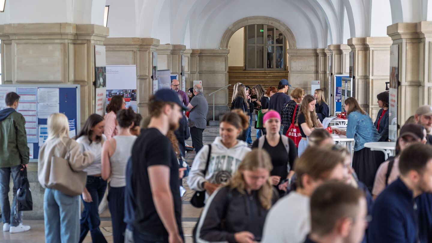 Menschen in einem hellen, gewölbten Gang mit Informationsständen an den Seiten