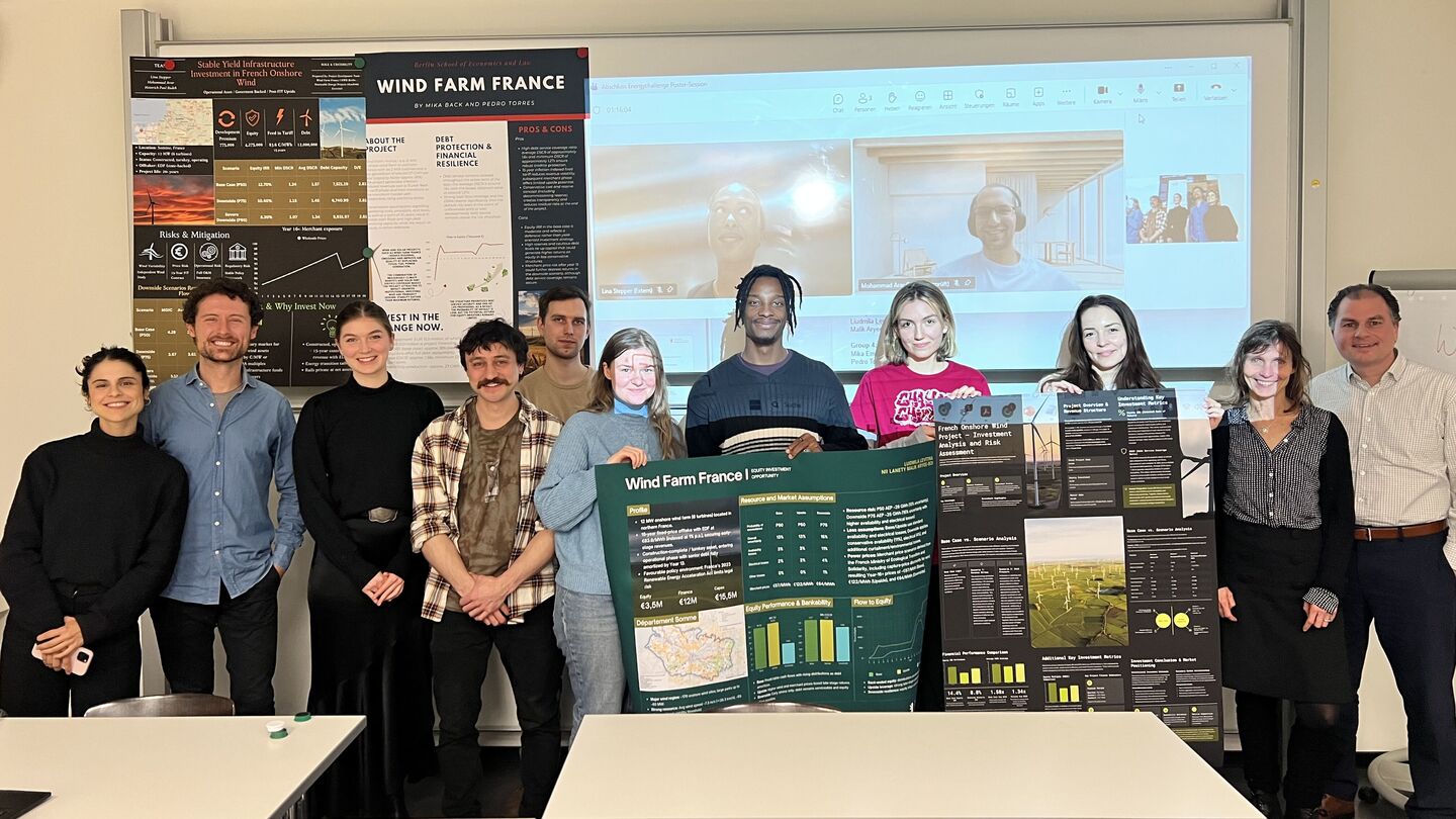 Group of people standing in a classroom holding posters about wind farms with a video call projected on the wall behind them