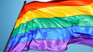 [Translate to English:] Regenbogenflagge flattert im Wind vor blauem Himmel. Foto: © mbolina/iStock/Getty Images Plus