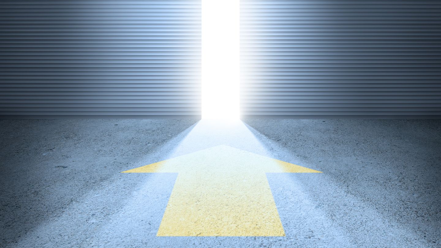 A yellow arrow on the asphalt points to a half-opened gate through which bright sunlight falls in. Photo: © olaser/Getty Images/iStockphoto