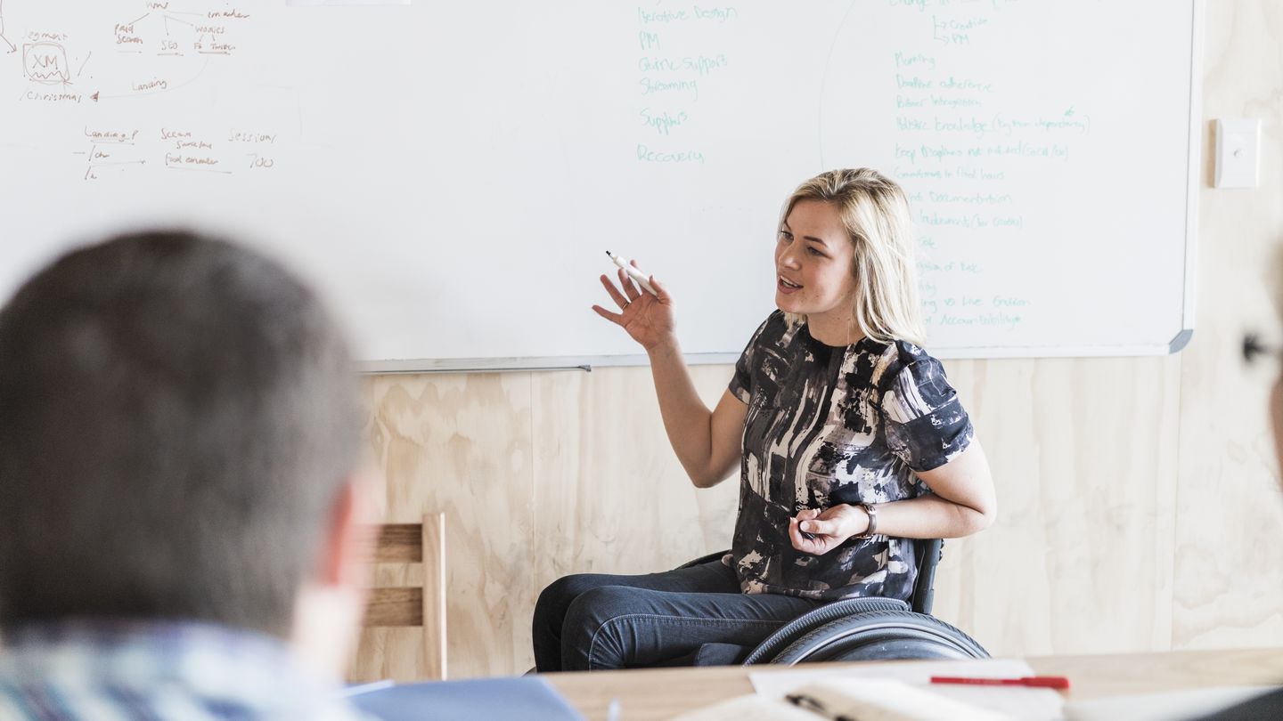 Studierende im Rollstuhl hält in einem Seminar einen Vortrag. Foto: © Portra/E+/Getty Images