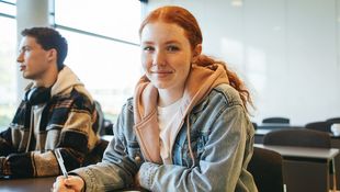 Schülerin sitzt in einem Klassenraum an einem Tisch.