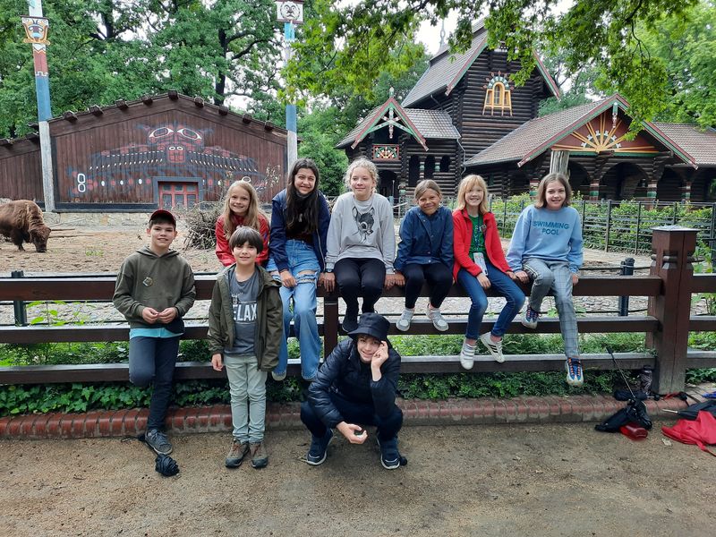 Ferienbetreuung 2021: Acht Kinder von Angehörigen der HWR Berlin und eine Betreuerin posieren im Stehen und Sitzen vor einem Gehege im Zoo Berlin. Foto: Carlo Just