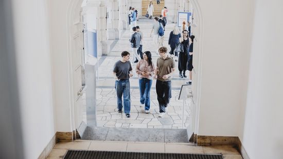 Studierende gehen durch einen gewölbten Durchgang in einem historischen Gebäude mit Steinboden