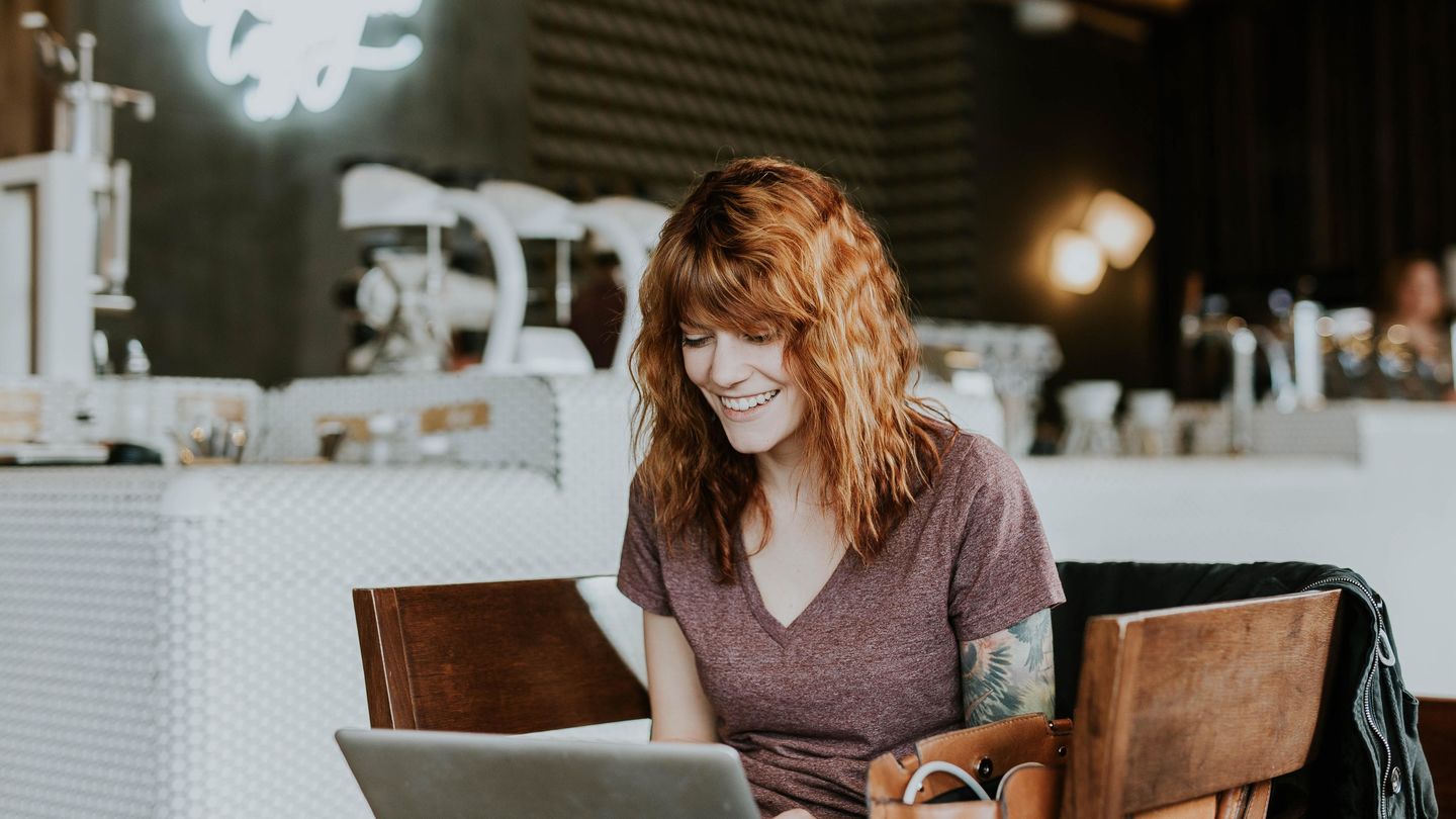 Eine junge Frau im grauen T-Shirt und mit schulterlangem Haar sitzt in einem Coffeeshop am Laptop. Foto: Brooke Cagle / Unsplash