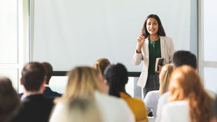 Eine Professorin im Blazer steht bei einer Vorlesung vor den Studierenden. Foto: © piranka/ Getty Images/ E+