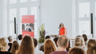 Frau in rotem Kleid spricht zu einem größeren Publikum.