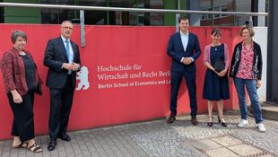 Staatssekretär und Personen aus der Hochschulleitung vor roter Wand mit HWR Berlin Logo