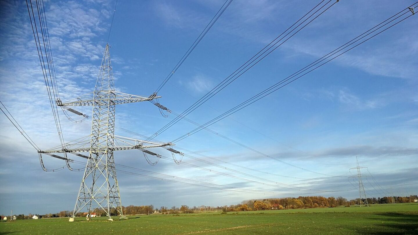 Hochspannungsmast mit mehreren Stromleitungen über einer grünen Wiese unter blauem Himmel