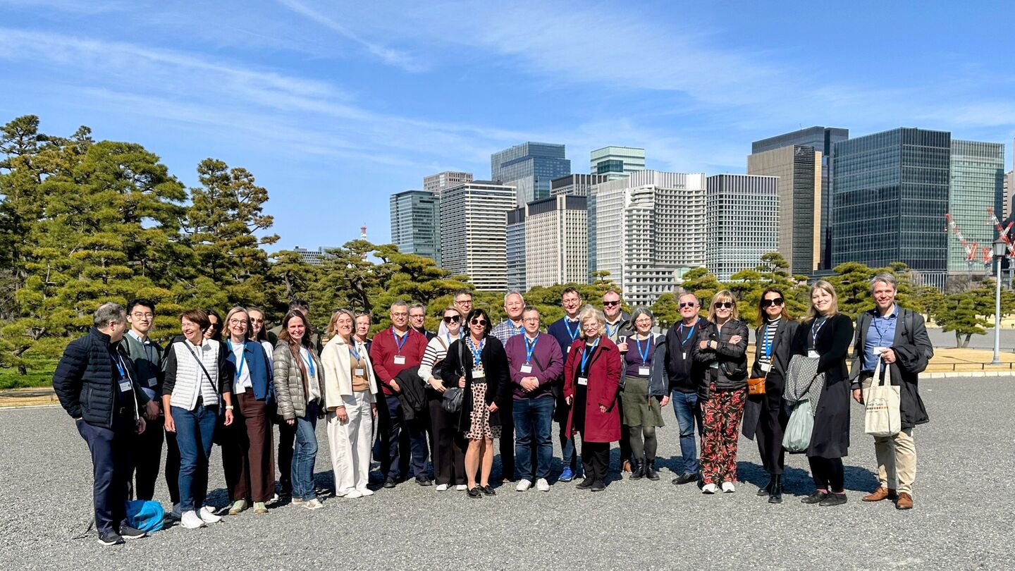 Gruppe von Menschen steht im Freien vor einer Stadt mit Hochhäusern und Bäumen im Hintergrund