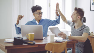 High Five: Zwei Studierende sitzen zuhause vor dem Rechner und freuen sich, weil sie eine Zulassung zum Studium erhalten haben. Foto: © Kondoros Eva Katalin/Getty Images/E+