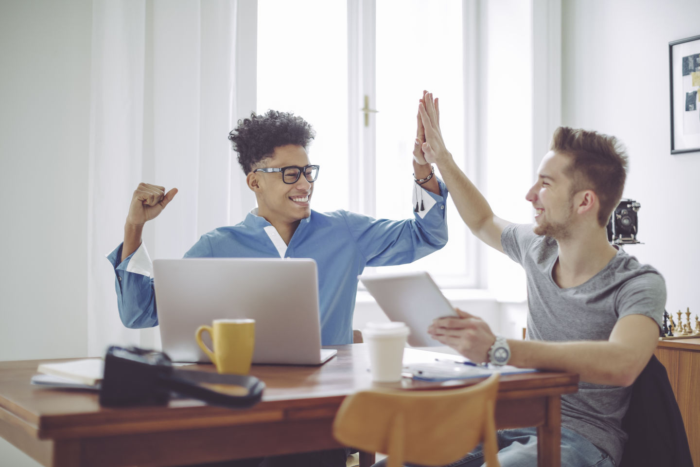 High Five: Two students are sitting at home in front of their computers, excited because they have been admitted to the university. Foto: © Kondoros Eva Katalin/Getty Images/E+