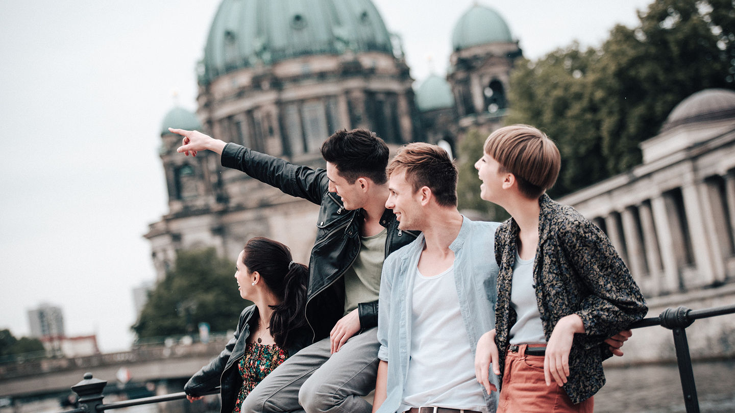 Two female and two male exchange students lean against a railing on the Spree. The dome of Berlin Cathedral can be seen in the background. Foto: © franckreporter/E+/Getty Images