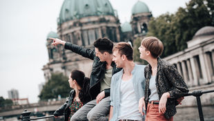 Two female and two male exchange students lean against a railing on the Spree. In the background, the dome of Berlin Cathedral can be seen. Photo: © franckreporter/E+/Getty Images
