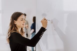 Master-Bewerbung an der HWR Berlin: Eine Studierende lächelt in die Kamera, dahinter sind zwei weibliche und zwei männliche Studierende im Gespräch zu sehen. Foto: © LumiNola/E+/Getty Images