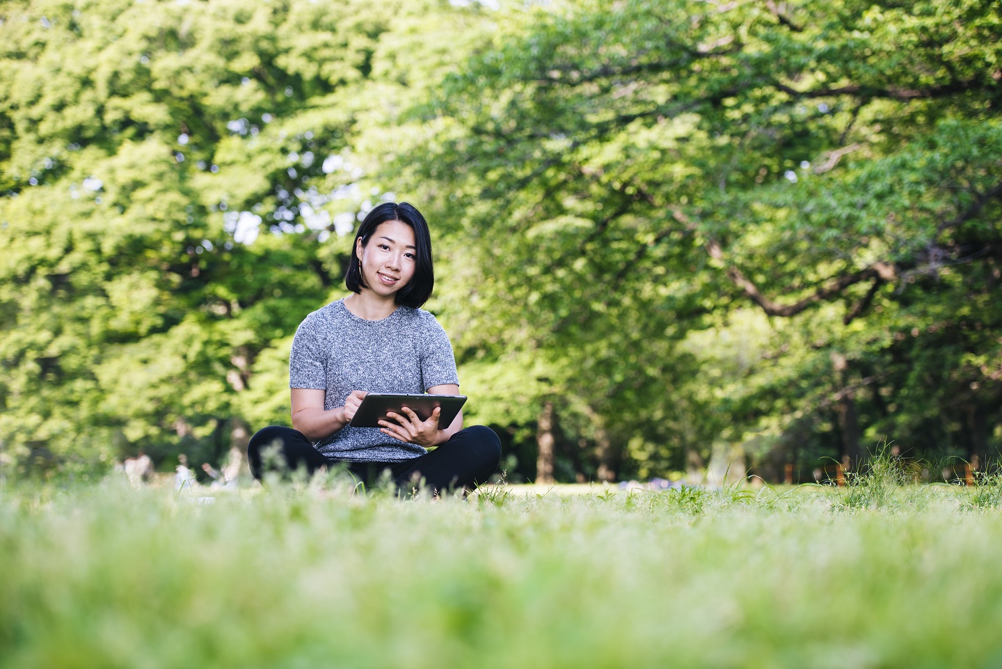 Junge Frau sitzt mit einem Tablet auf einer Wiese. © AzmanL/Getty Images/E+