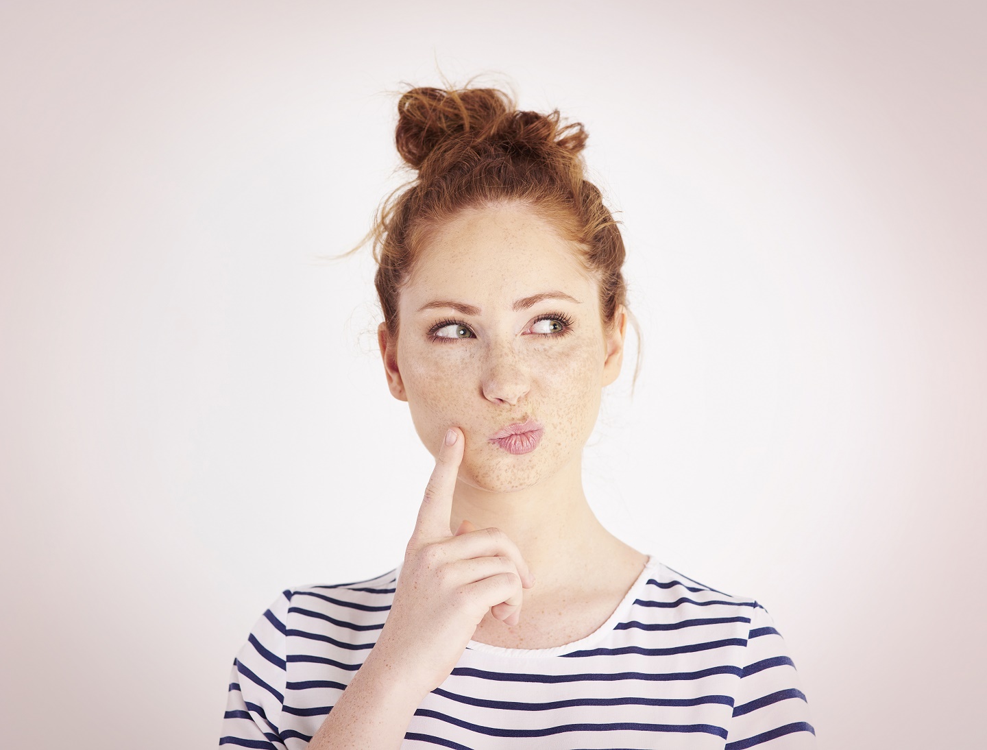 Find a degree programme: Young woman with pinned-up hair ponders and taps her cheek with her index finger. Photo: © Gpoint Studio/Getty Images/iStockphoto